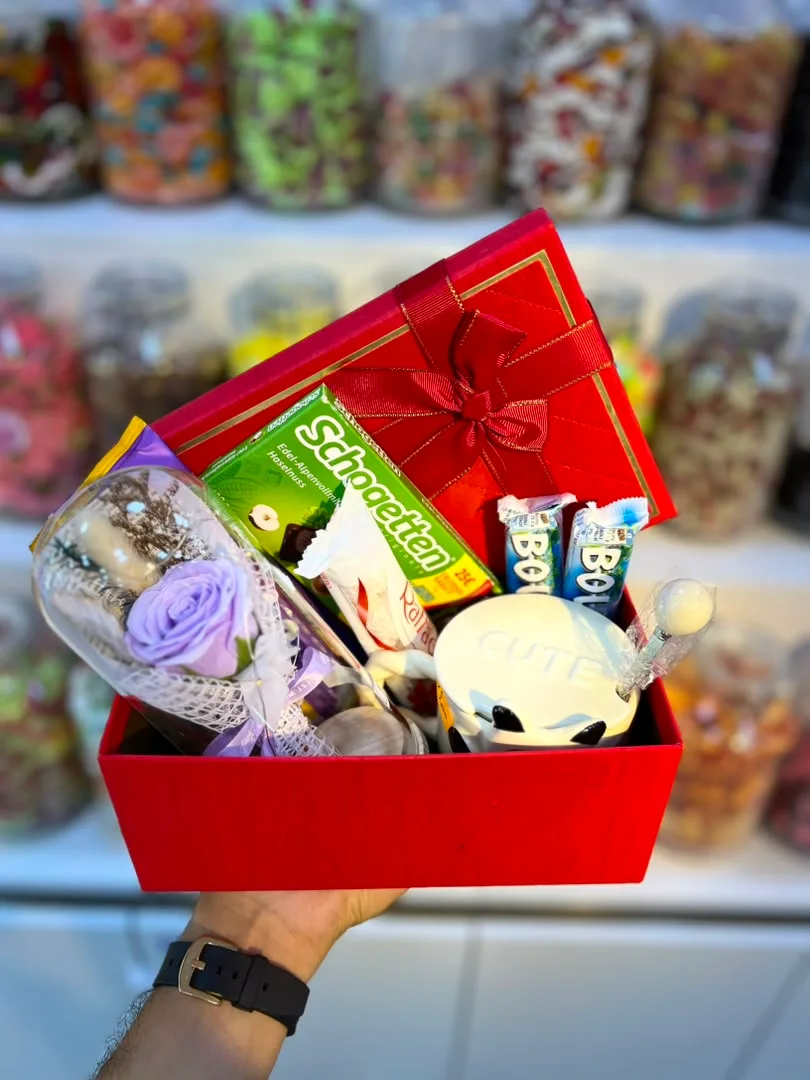 بوكس هدايا يحتوي على الشوكولاتة والحلويات ووردة جميلة، مقدّم داخل علبة حمراء أنيقة. 🍫🌹