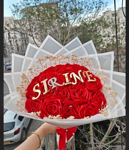 باقة رائعة من الورود الحمراء، مزينة بزهور بيضاء صغيرة وتحمل عبارة مخصصة. ❤️✨